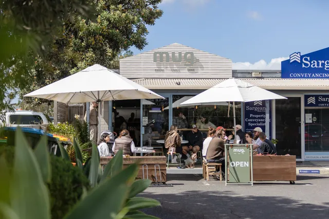 mug. café exterior with customers dining under white umbrellas on a sunny day in Cowes