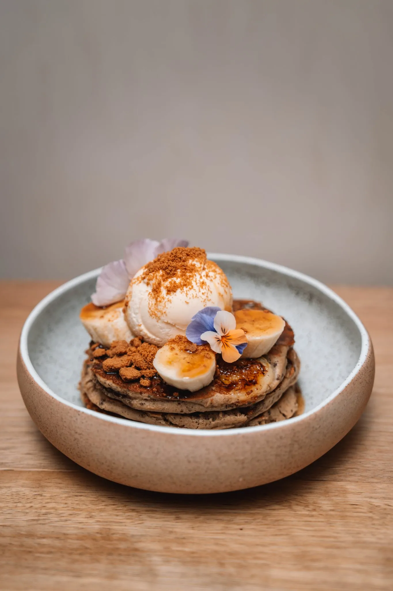 Buckwheat pancakes with vanilla ice cream, banana, cinnamon crumble and edible flowers in a ceramic bowl