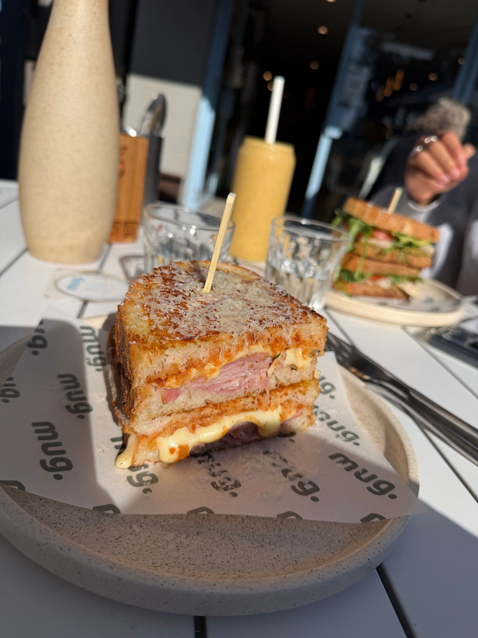 Toasted toastie on mug. branded wrapper with drinks and another diner visible in the background