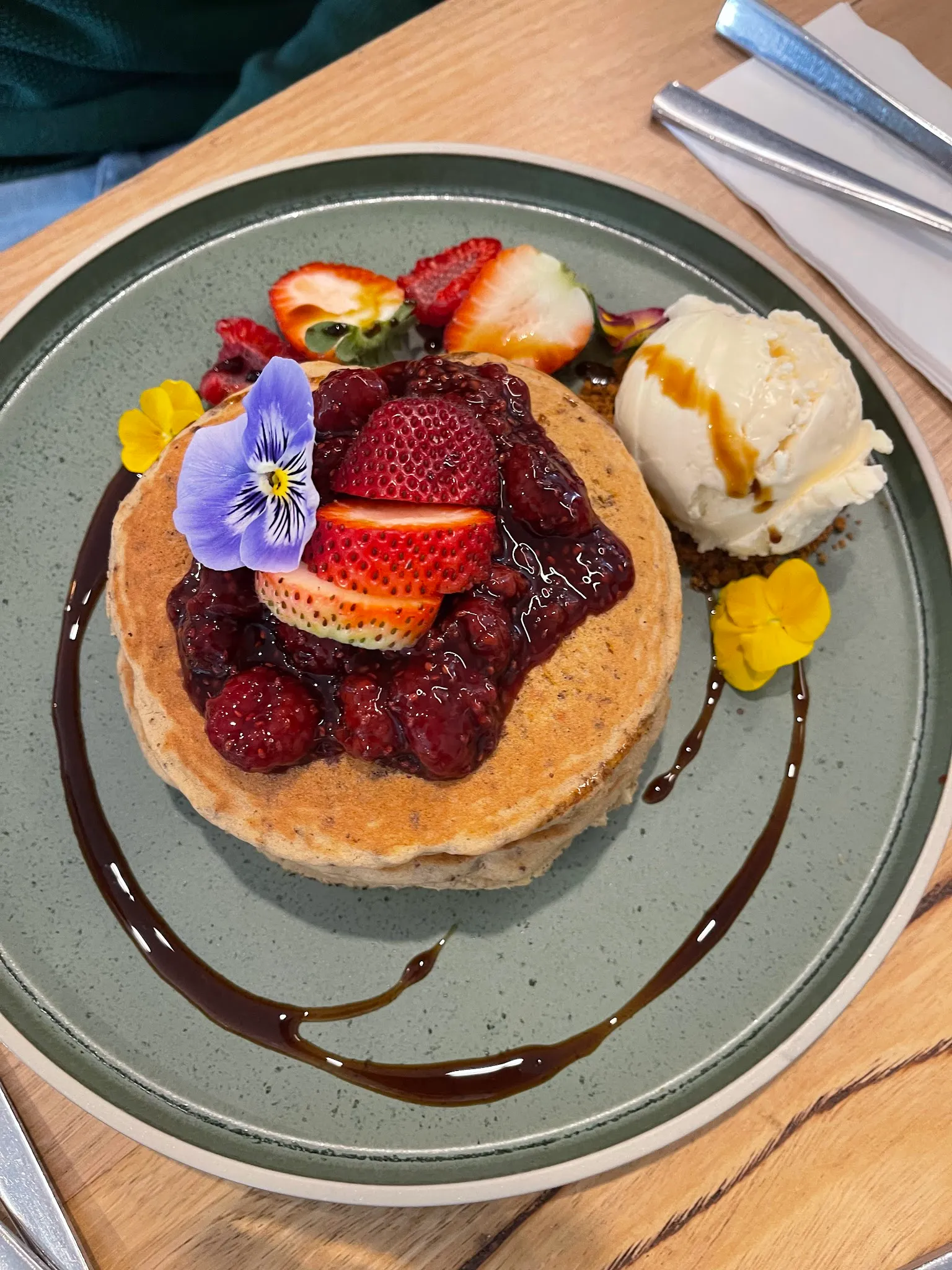 Berry pancakes with strawberry compote, ice cream and edible flowers on a sage green plate