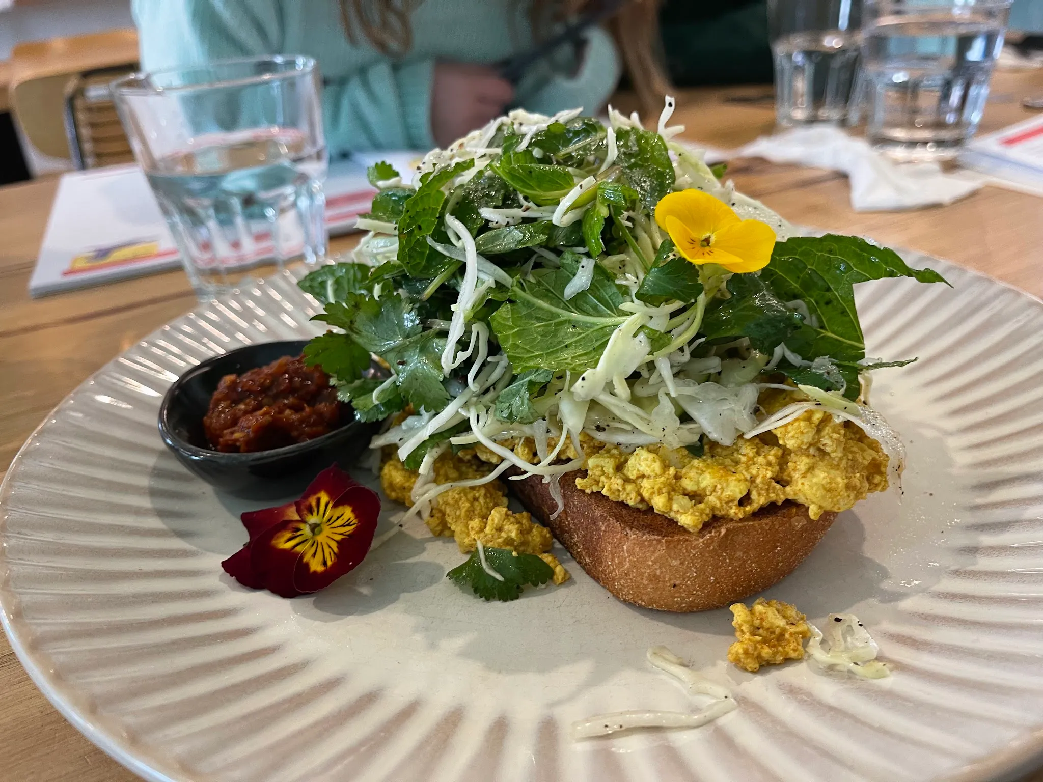 Tofu scramble on sourdough with herb salad and edible flowers, chilli sambal on the side