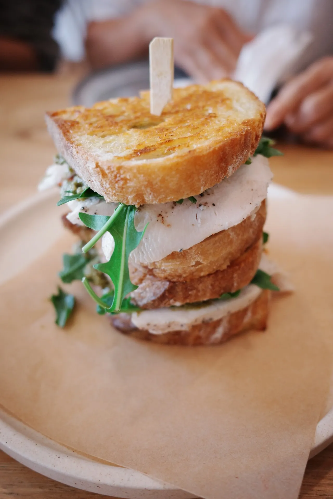 Tall stacked chicken toastie on sourdough with person's hands visible in background