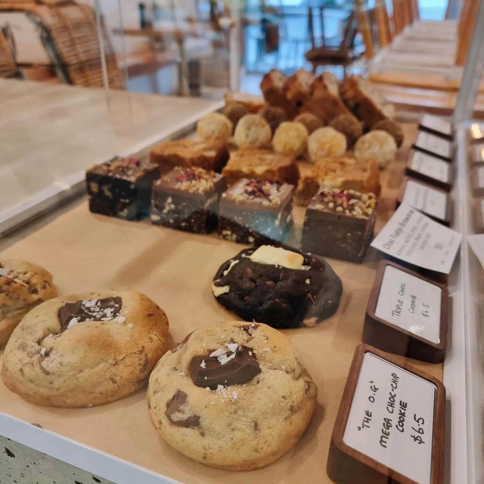 Glass counter display of house-made cookies, raw fudge slices and sweet treats with café interior visible behind