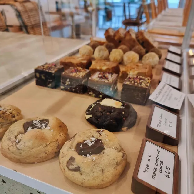 Glass counter display of house-made cookies, raw fudge slices and sweet treats with café interior visible behind