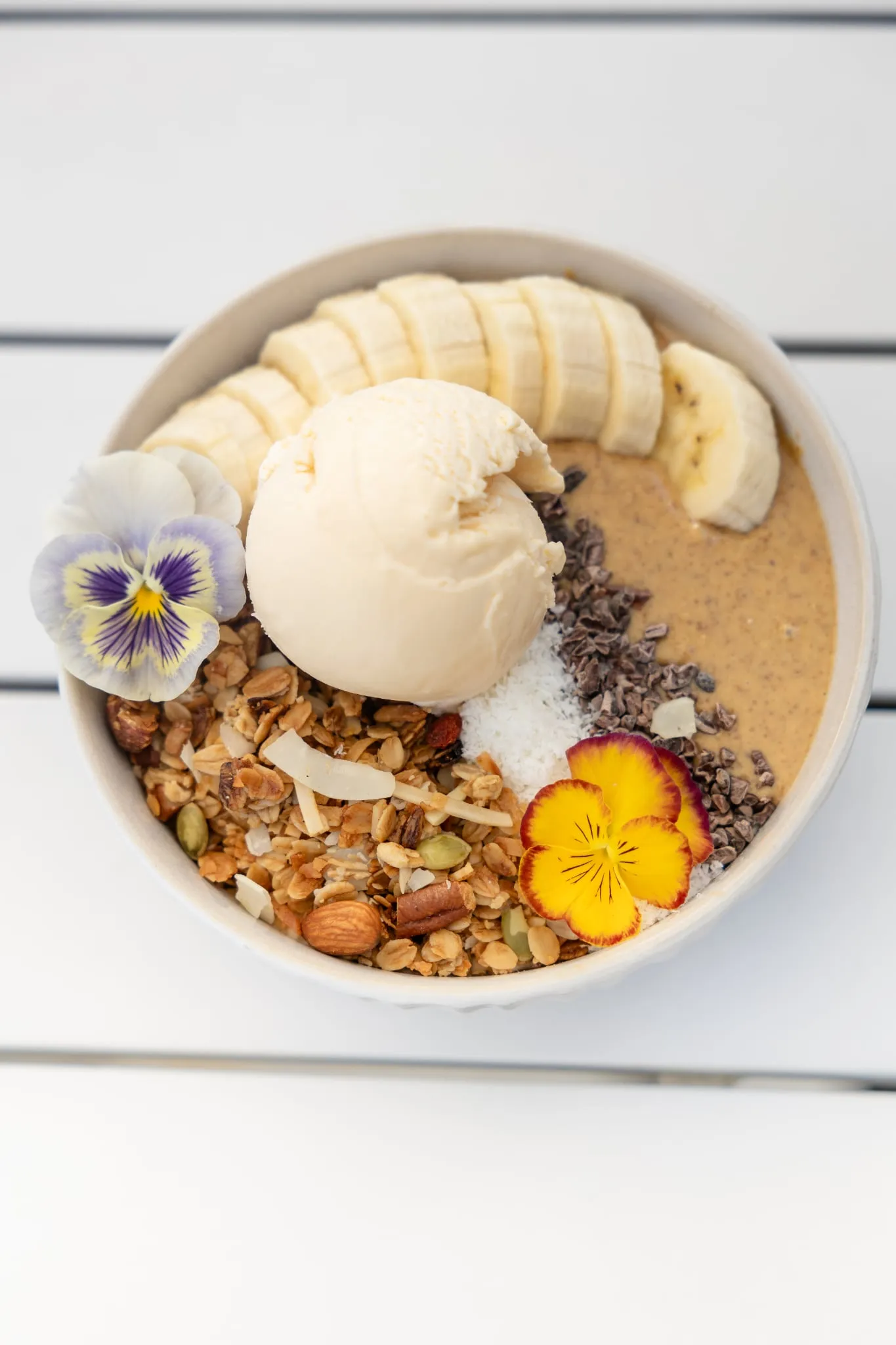 Smoothie bowl with banana, granola, coconut, cacao nibs, ice cream and edible flowers