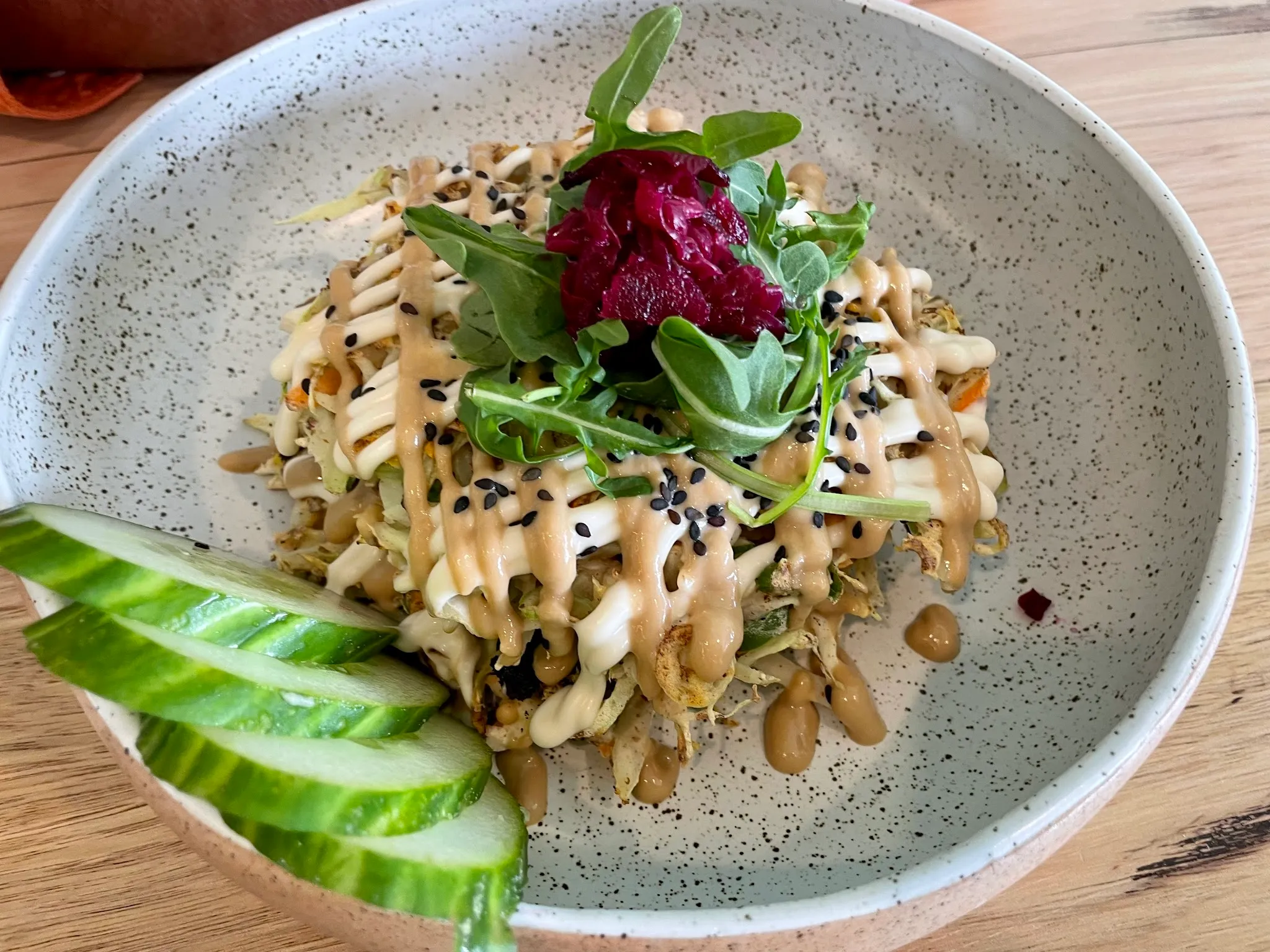 Noodle bowl with tahini drizzle, beetroot, rocket and cucumber in a white speckled ceramic bowl