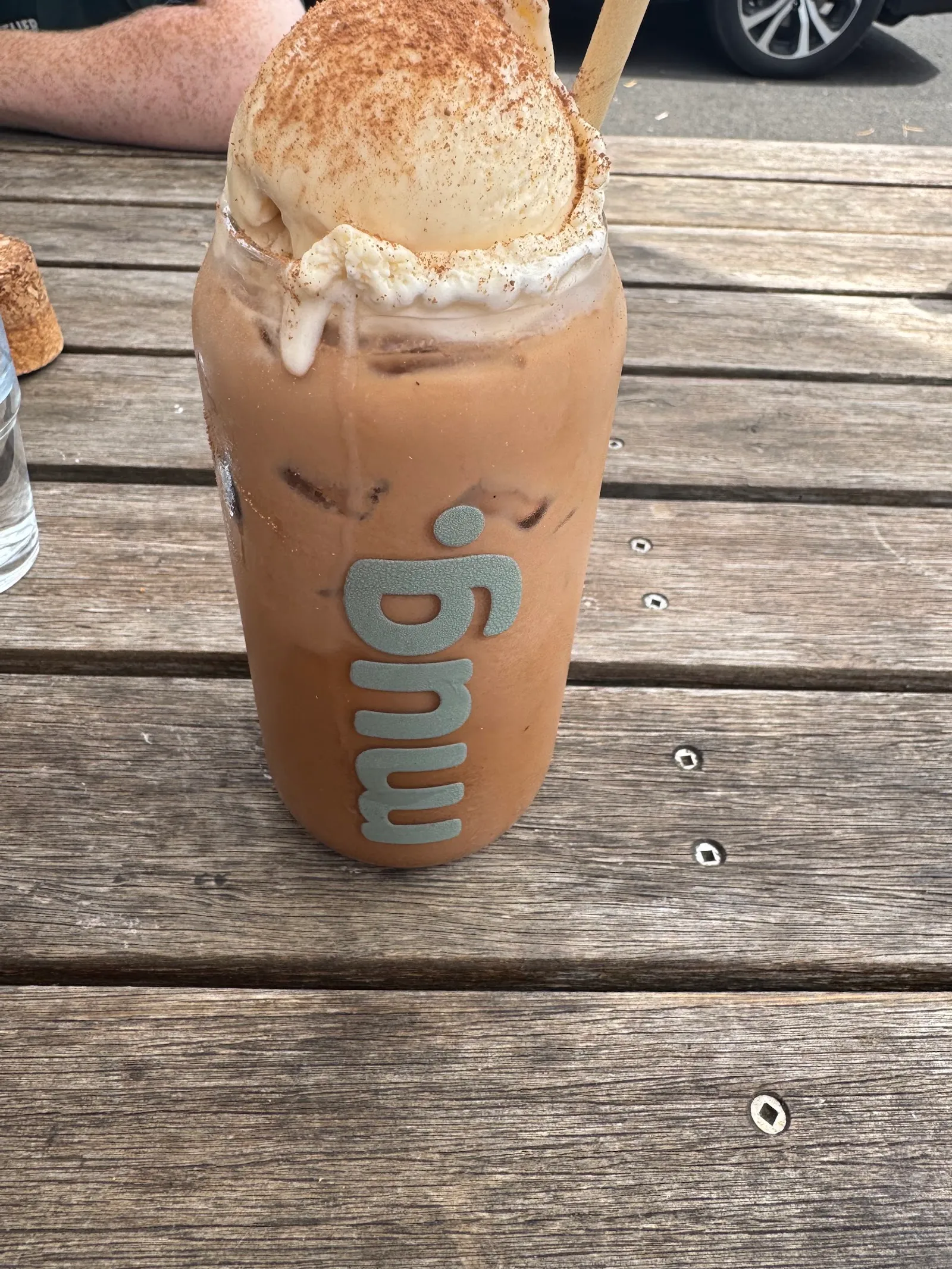 Iced chilli choc chai with toasted marshmallow in a mug. branded glass on an outdoor timber table