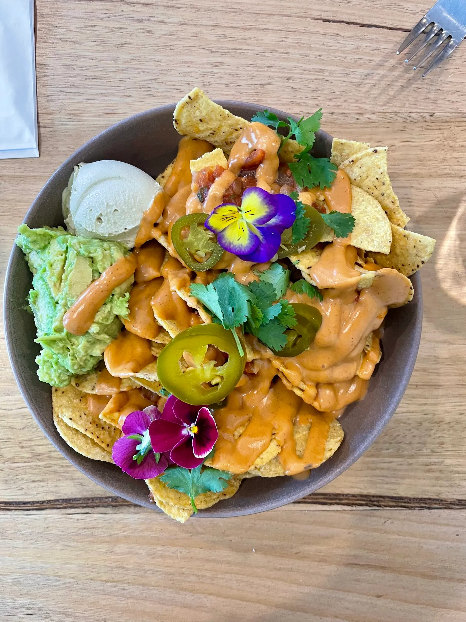 Vegan nachos bowl with cashew cheese sauce, guacamole, jalapeños and edible flowers in a grey ceramic bowl